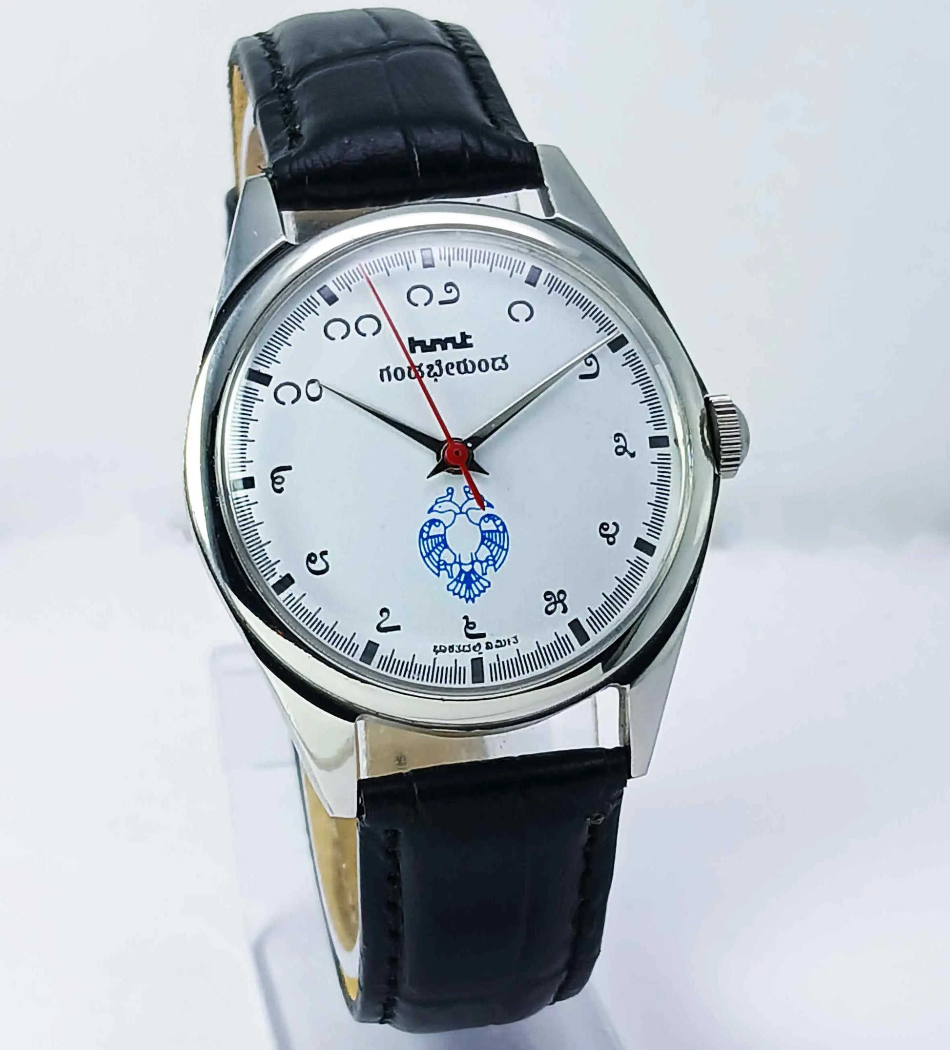 Wristwatch with black leather strap and white dial on a light gray background