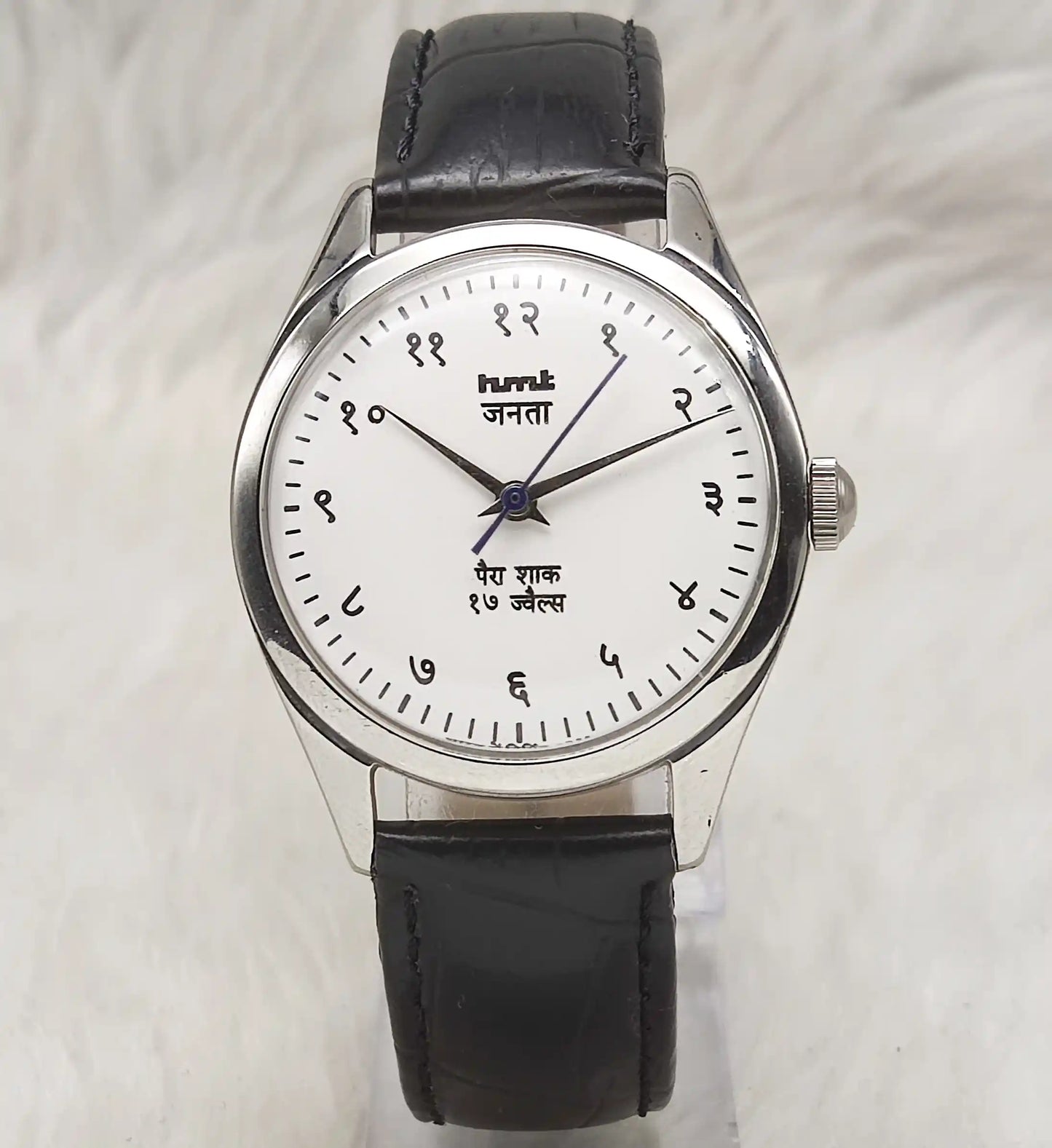 Wristwatch with black leather strap and white dial on a light gray background