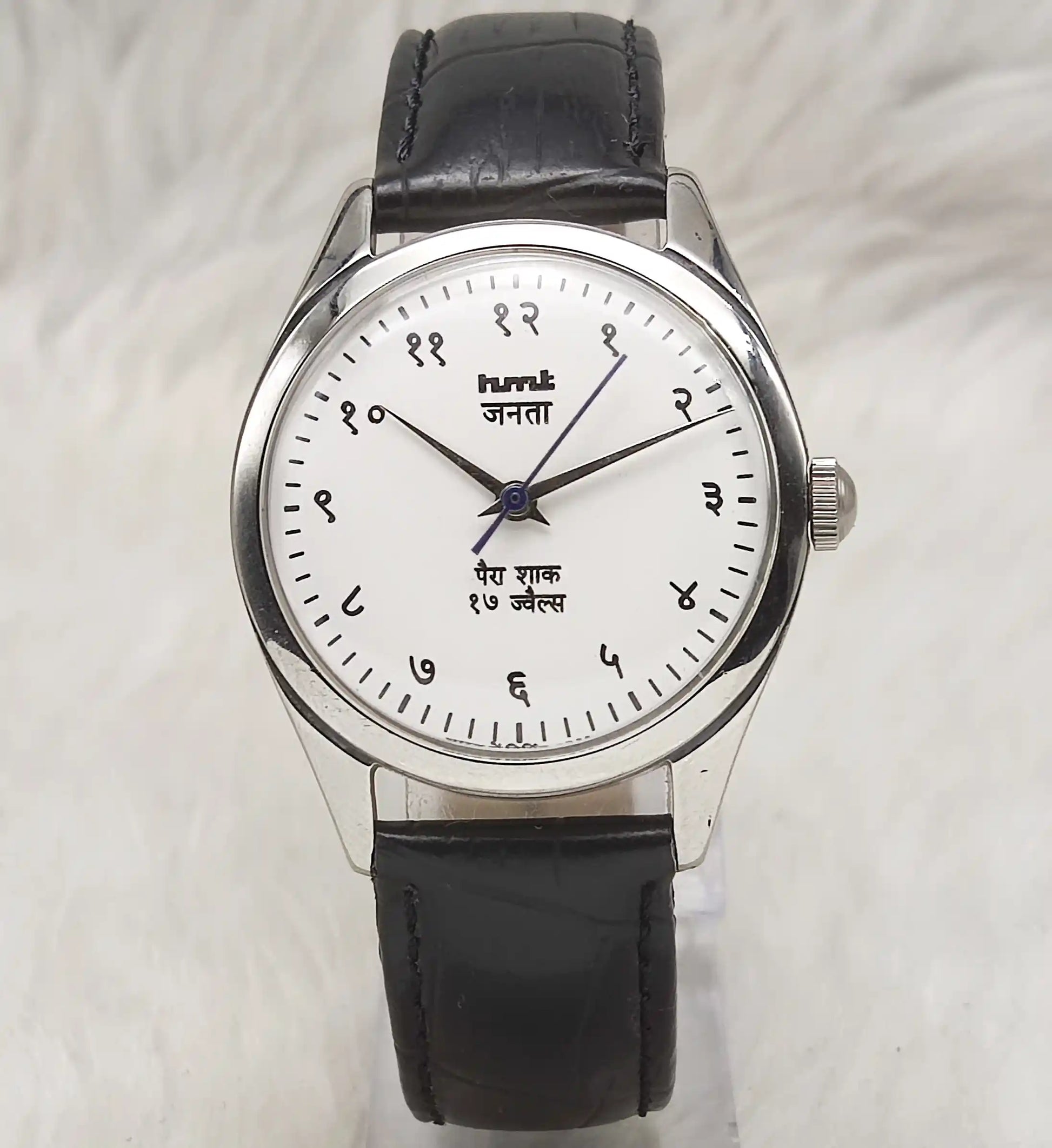 Wristwatch with black leather strap and white dial on a light gray background