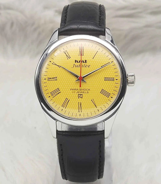Watch with a yellow face and black leather strap on a light gray background